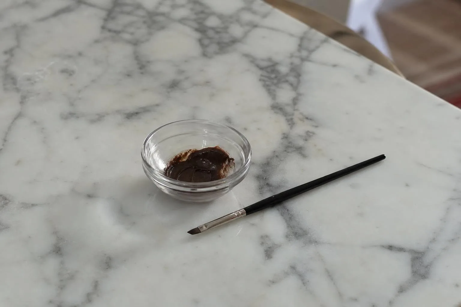 Cuenco con tinte de cejas y pincel fino sobre una mesa de mármol