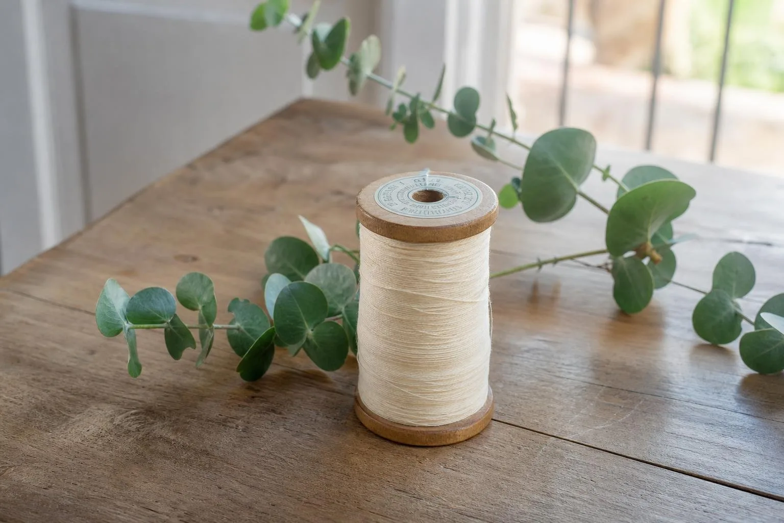 Carrete de hilo sobre una mesa de madera con eucalipto