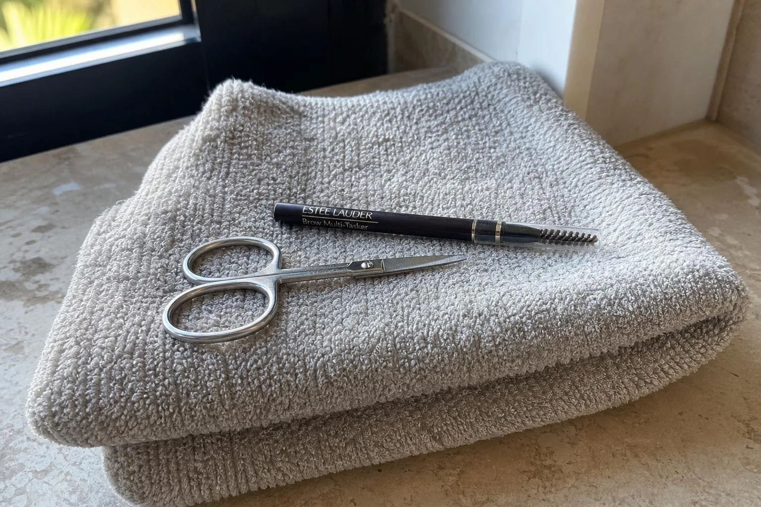 Tijeras pequeñas y lápiz de cejas sobre una toalla doblada