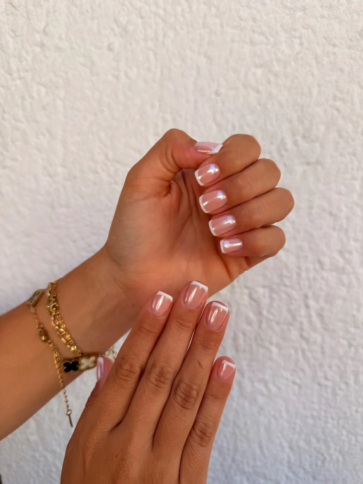 Manos con uñas cortas rosadas de acabado perlado con borde blanco y pulseras doradas