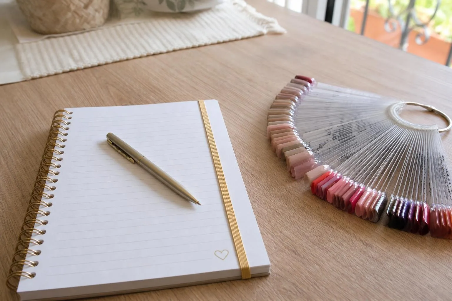 Cuaderno y bolígrafo junto a muestras de diseños de uñas