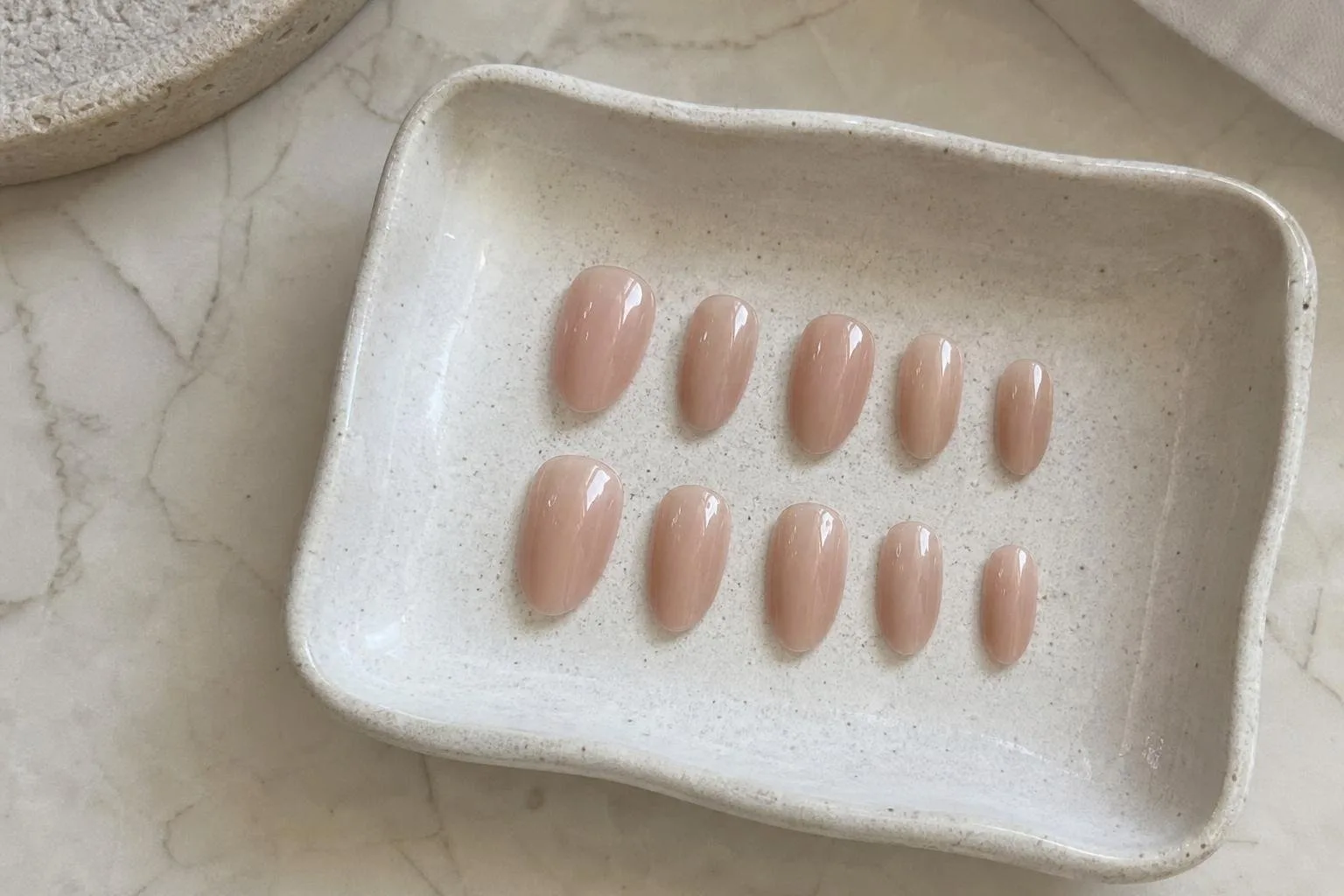 Uñas de gel constructor nude terminadas sobre una bandeja de cerámica