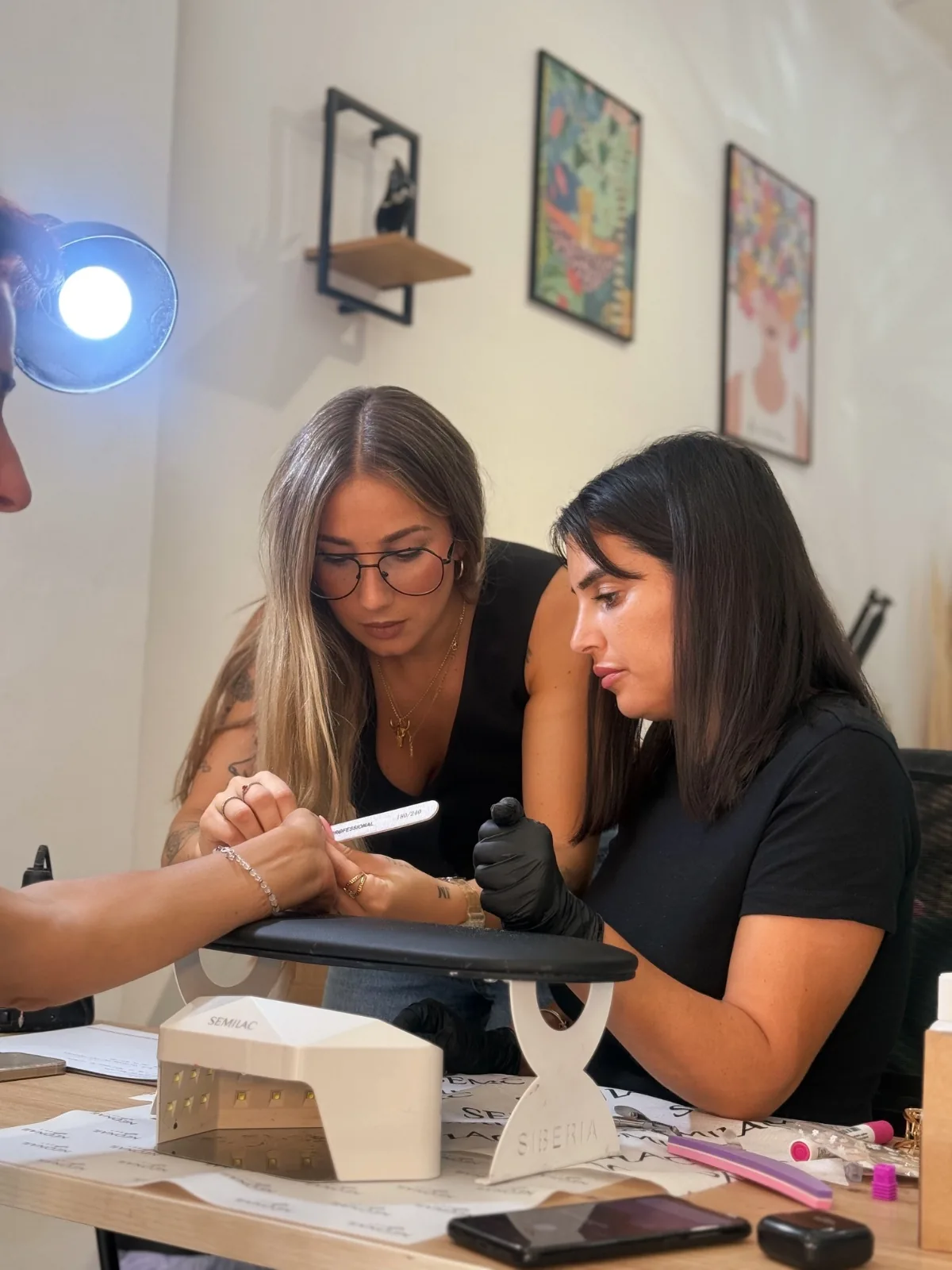 Dos profesionales trabajando en una manicura durante una formación, con lámpara y limas en la mesa